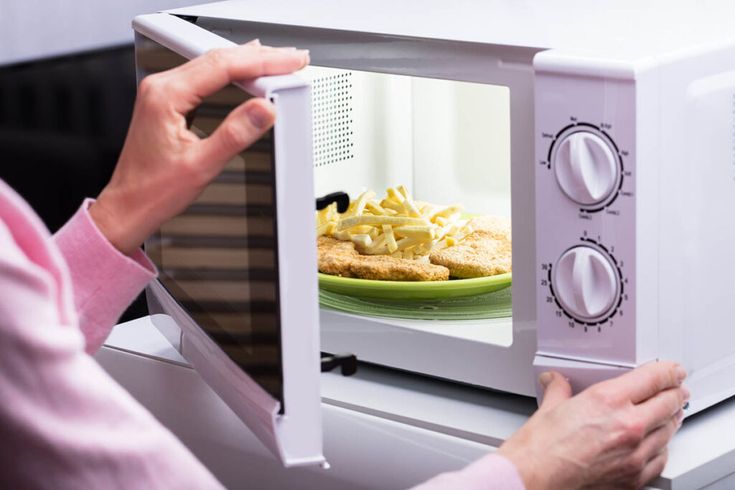 Mãos de mulher abrindo a porta do forno de micro-ondas